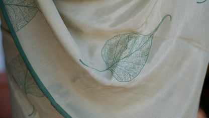 Muslin handcrafted, naturally dyed saree in a shade of beige with green border and pipal leaf motif.