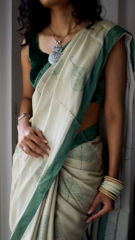 Muslin handcrafted, naturally dyed saree in a shade of beige with green border and pipal leaf motif.