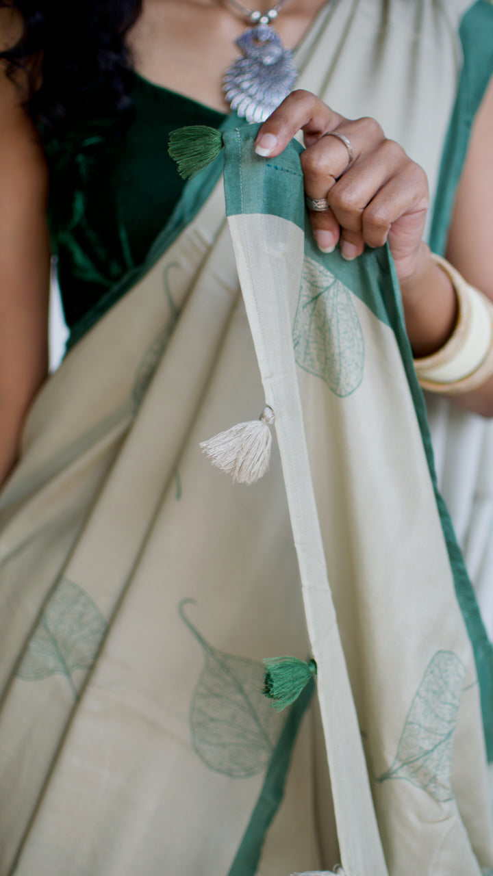 Muslin handcrafted, naturally dyed saree in a shade of beige with green border and pipal leaf motif.