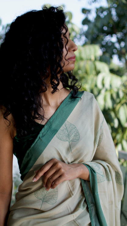 Muslin handcrafted, naturally dyed saree in a shade of beige with green border and pipal leaf motif.